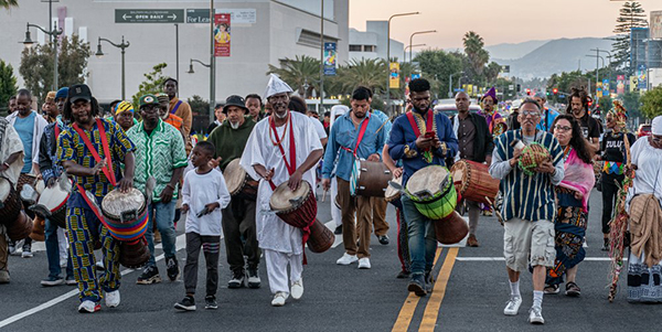 A photo of the 100 Drums for Peace and Healing, a procession of drummers playing in the street.